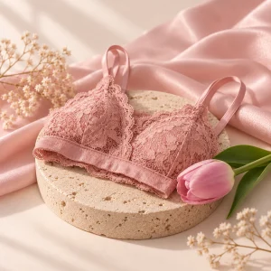 Bralette de encaje rosado sobre un pedestal de travertino junto a un tulipán, con satén rosado de fondo